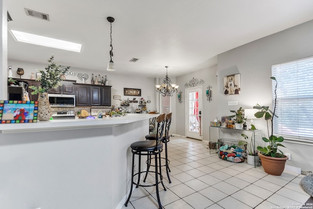 kitchen featuring a chandelier, dark brown cabinets, pendant lighting, light tile patterned flooring, and a kitchen breakfast bar