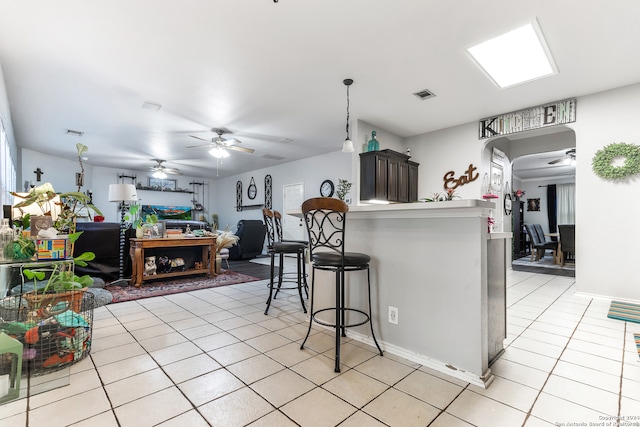 kitchen with light tile patterned floors, hanging light fixtures, a kitchen bar, ceiling fan, and kitchen peninsula