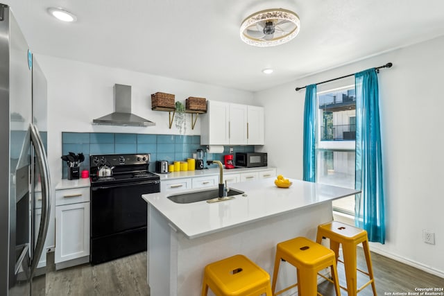 kitchen featuring tasteful backsplash, a kitchen breakfast bar, black appliances, sink, and wall chimney range hood