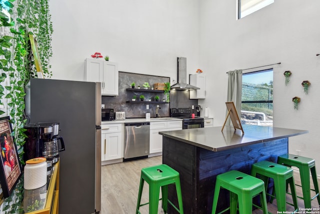 kitchen with white cabinetry, light hardwood / wood-style flooring, black appliances, a breakfast bar, and wall chimney exhaust hood