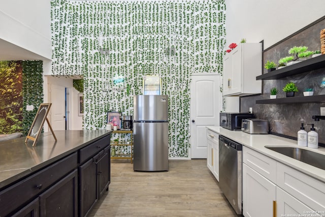 kitchen with tasteful backsplash, sink, appliances with stainless steel finishes, white cabinets, and light hardwood / wood-style floors