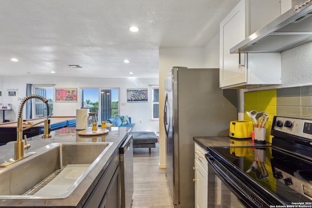 kitchen with light wood-type flooring, black range with electric stovetop, white cabinetry, sink, and tasteful backsplash