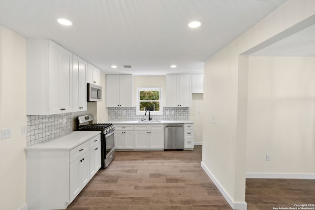 kitchen featuring decorative backsplash, white cabinets, light wood-type flooring, stainless steel appliances, and sink