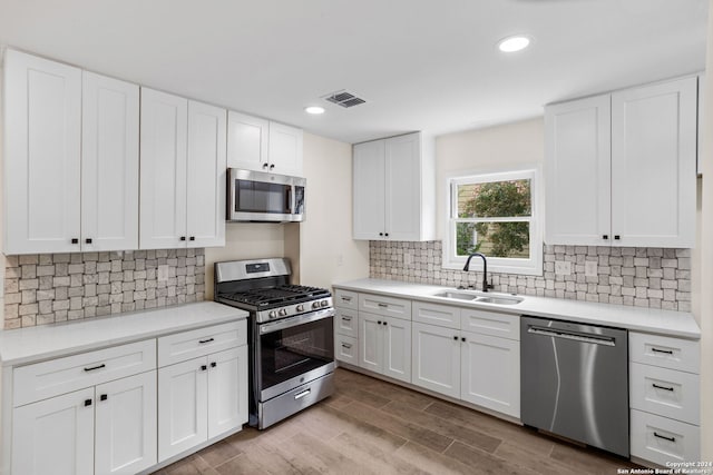 kitchen with stainless steel appliances, white cabinets, sink, tasteful backsplash, and light hardwood / wood-style floors