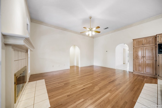 unfurnished living room featuring a tile fireplace, ornamental molding, ceiling fan, and light hardwood / wood-style floors