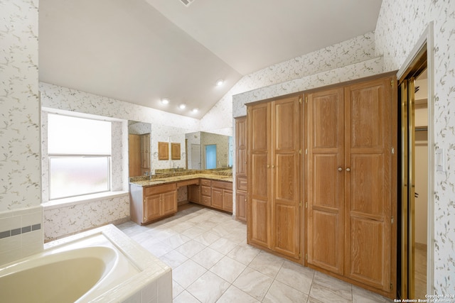 bathroom with lofted ceiling, tile patterned floors, tiled bath, and vanity