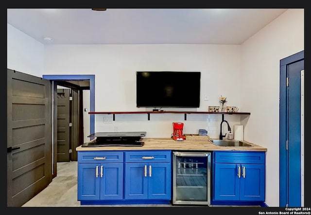 bar with beverage cooler, blue cabinets, butcher block counters, and sink