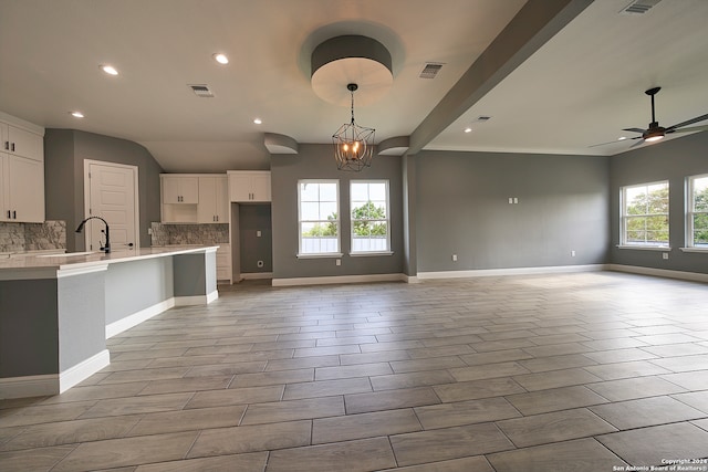 unfurnished living room featuring ceiling fan with notable chandelier, lofted ceiling with beams, light tile patterned floors, and a wealth of natural light