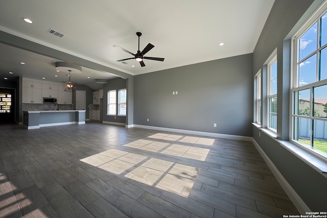 unfurnished living room with ceiling fan, crown molding, wood-type flooring, and a wealth of natural light