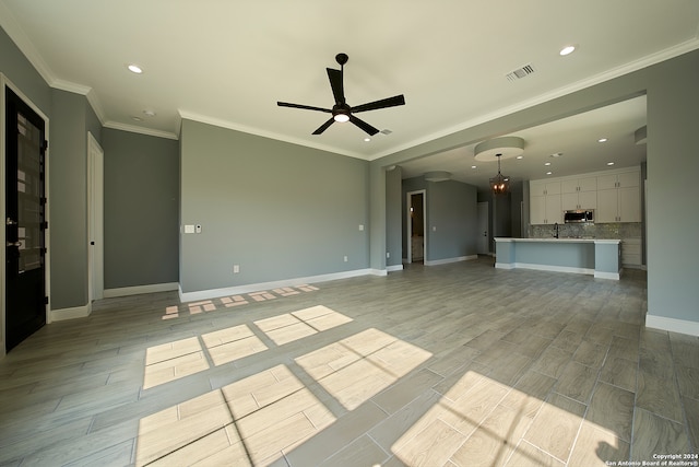 unfurnished living room featuring ceiling fan, sink, light hardwood / wood-style floors, and crown molding