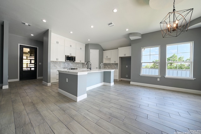 kitchen with white cabinets, backsplash, an island with sink, sink, and light wood-type flooring