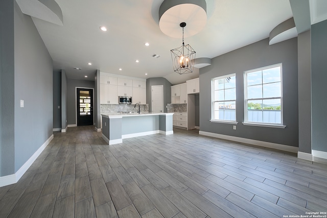 kitchen featuring white cabinets, a center island with sink, tasteful backsplash, and a wealth of natural light