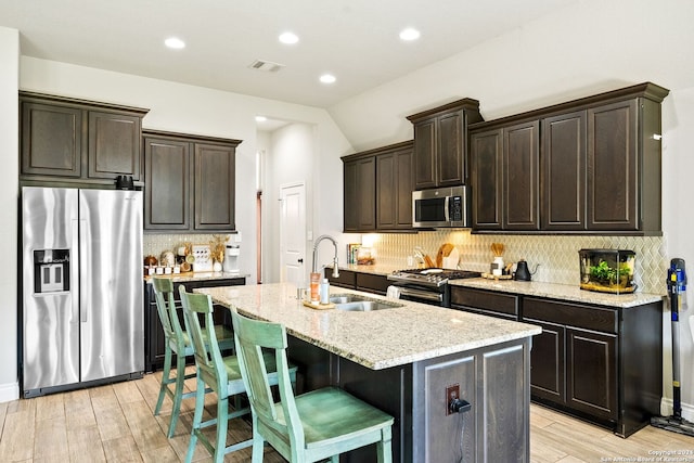 kitchen featuring tasteful backsplash, a kitchen island with sink, stainless steel appliances, and dark brown cabinetry