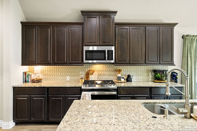 kitchen with appliances with stainless steel finishes, sink, tasteful backsplash, dark brown cabinetry, and light stone counters