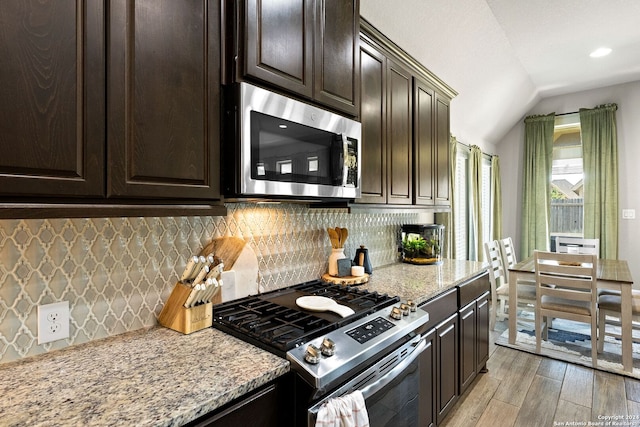 kitchen featuring light hardwood / wood-style flooring, light stone counters, lofted ceiling, appliances with stainless steel finishes, and tasteful backsplash