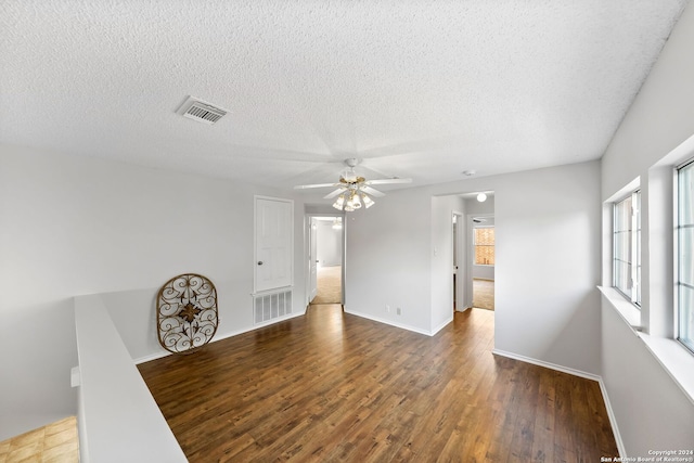 empty room with a textured ceiling, wood finished floors, visible vents, and baseboards