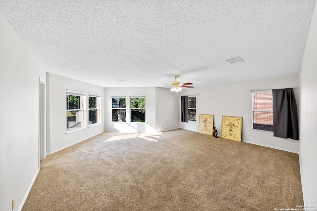 carpeted spare room featuring a textured ceiling, ceiling fan, visible vents, and a healthy amount of sunlight