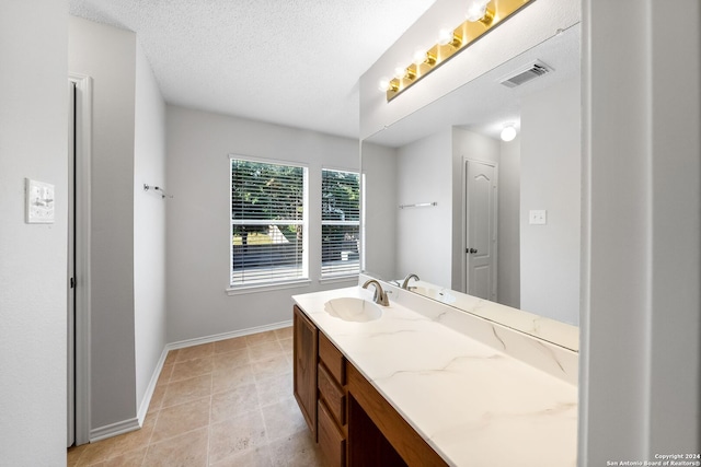 bathroom with a textured ceiling, vanity, visible vents, baseboards, and tile patterned floors