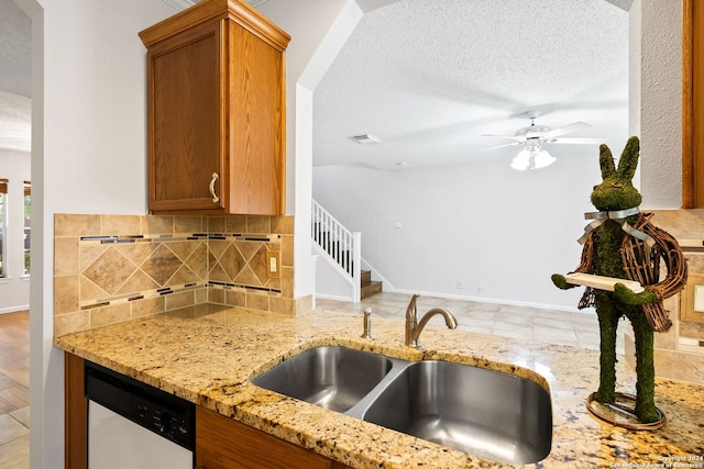 kitchen featuring a textured ceiling, white dishwasher, a sink, light stone countertops, and tasteful backsplash