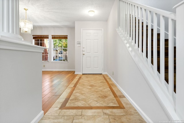 foyer entrance featuring a textured ceiling, an inviting chandelier, and baseboards