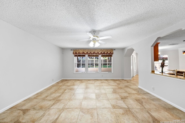 tiled empty room with arched walkways, ceiling fan, a textured ceiling, and baseboards