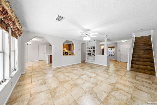 unfurnished living room with arched walkways, a healthy amount of sunlight, visible vents, and stairway