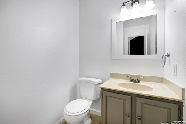 half bath with baseboards, vanity, and toilet