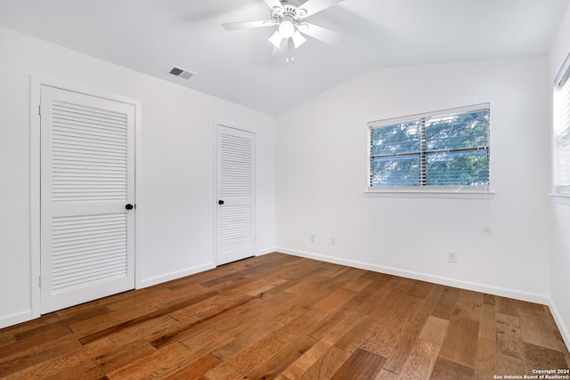 unfurnished bedroom with lofted ceiling, multiple closets, wood-type flooring, and ceiling fan