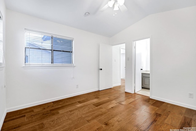 unfurnished bedroom featuring ensuite bathroom, a ceiling fan, vaulted ceiling, wood finished floors, and baseboards