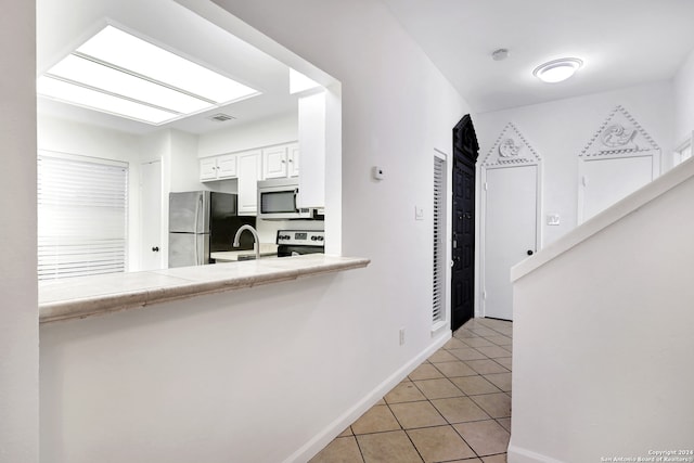 kitchen featuring light tile patterned floors, appliances with stainless steel finishes, tile countertops, white cabinetry, and kitchen peninsula