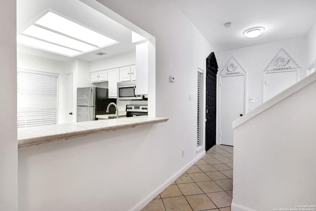 kitchen with light tile patterned floors, tile counters, white cabinets, appliances with stainless steel finishes, and a sink