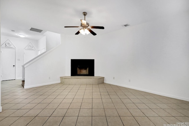 unfurnished living room featuring visible vents, a fireplace with raised hearth, baseboards, and ceiling fan
