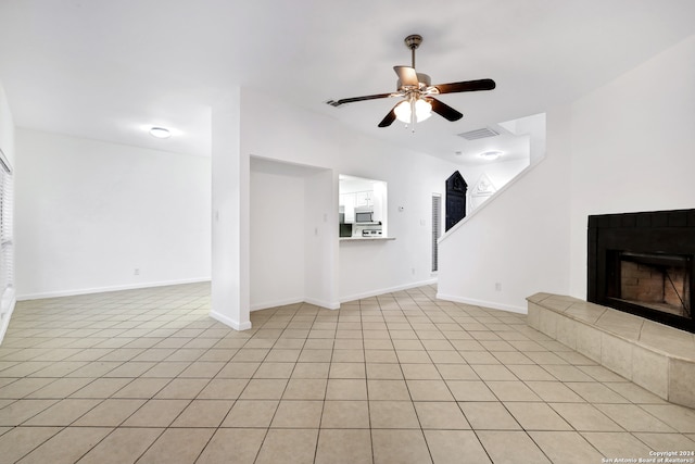 unfurnished living room with a tiled fireplace, light tile patterned flooring, and ceiling fan