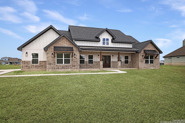 view of front of property with a front lawn, brick siding, a standing seam roof, and board and batten siding