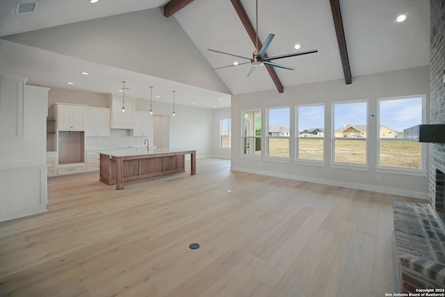 unfurnished living room with visible vents, beamed ceiling, light wood finished floors, a ceiling fan, and a sink