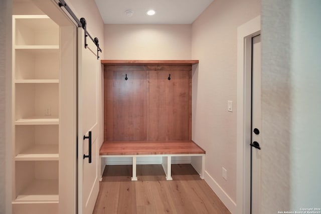 mudroom with baseboards, a barn door, built in shelves, and light wood-style flooring