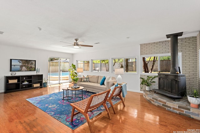 living room featuring ceiling fan, a wood stove, hardwood / wood-style flooring, and a wealth of natural light