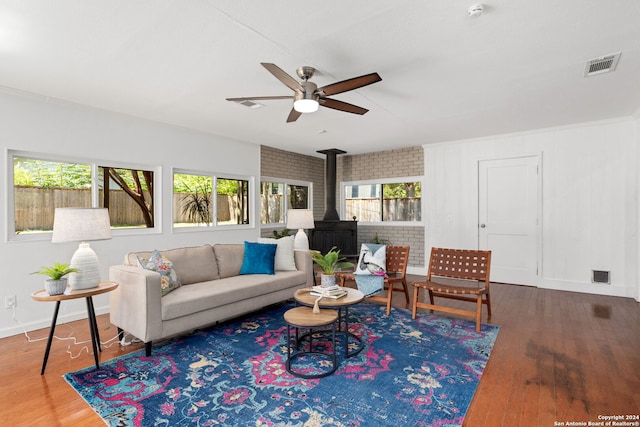 living room with ceiling fan, brick wall, hardwood / wood-style floors, and a wood stove