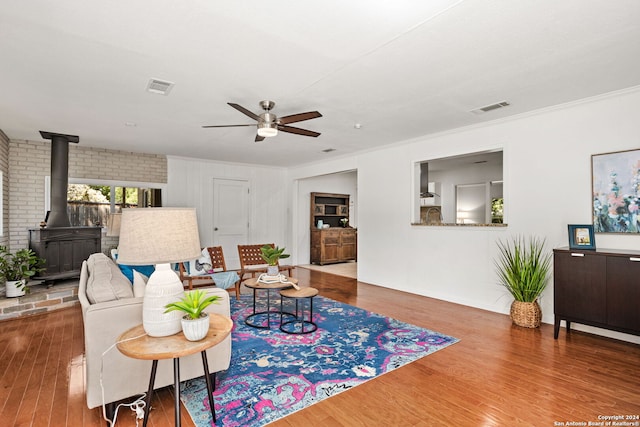 living room featuring crown molding, a wood stove, ceiling fan, wood-type flooring, and brick wall