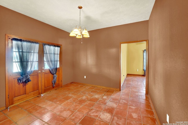 spare room featuring a notable chandelier, tile patterned floors, and a textured ceiling