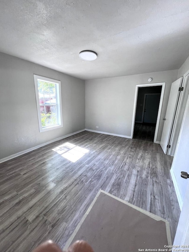 empty room with baseboards, a textured ceiling, and wood finished floors