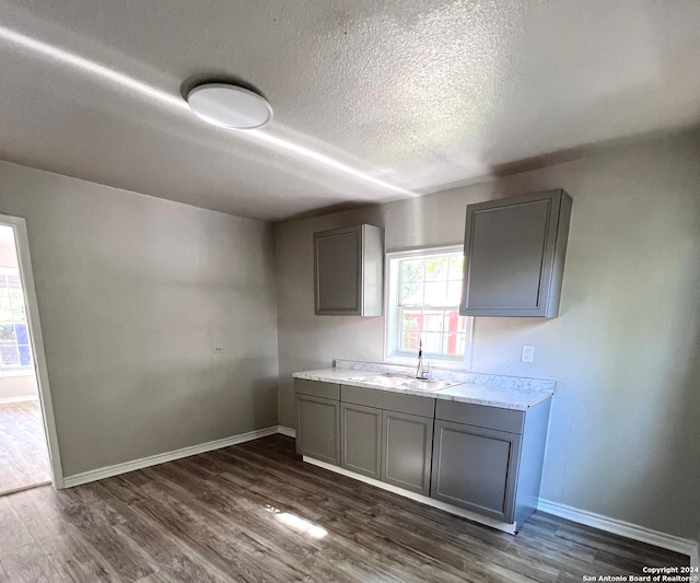 kitchen featuring a textured ceiling, dark hardwood / wood-style floors, light stone countertops, gray cabinets, and sink