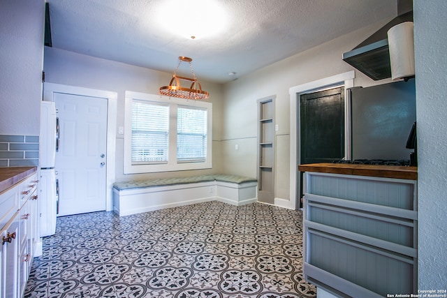 kitchen with a textured ceiling, white cabinetry, hanging light fixtures, stainless steel fridge, and tile patterned flooring