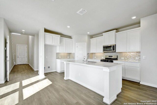 kitchen with sink, a center island with sink, appliances with stainless steel finishes, light hardwood / wood-style floors, and white cabinets