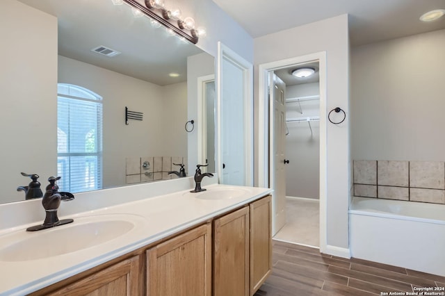 bathroom with a walk in closet, visible vents, a sink, and a garden tub