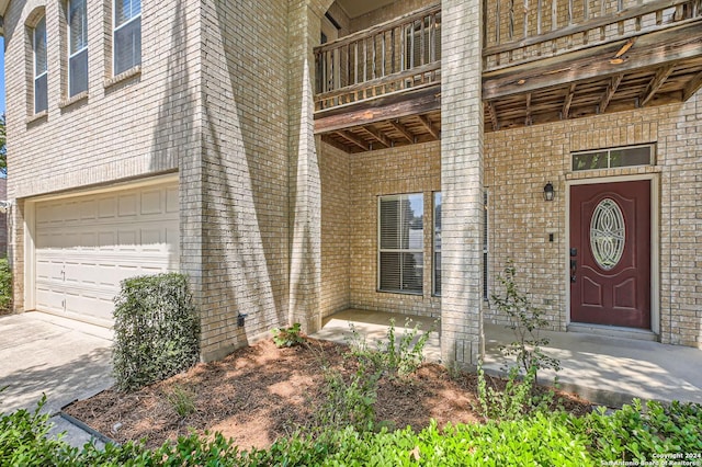 doorway to property with an attached garage, a balcony, concrete driveway, and brick siding