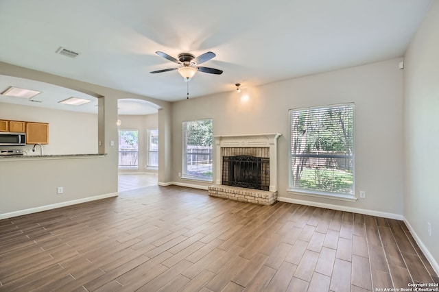 unfurnished living room featuring ceiling fan, a fireplace, sink, and hardwood / wood-style floors