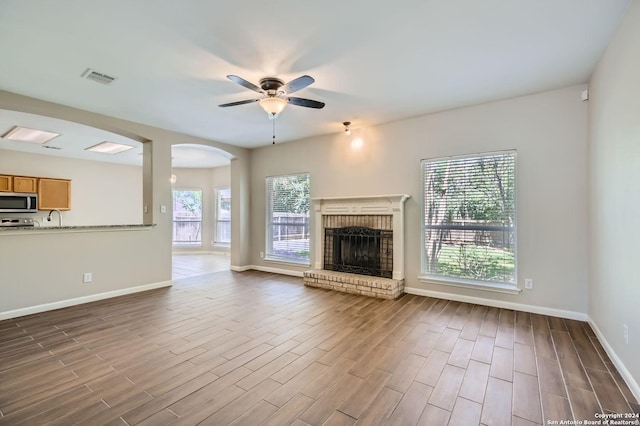 unfurnished living room featuring ceiling fan, wood finished floors, visible vents, baseboards, and a brick fireplace