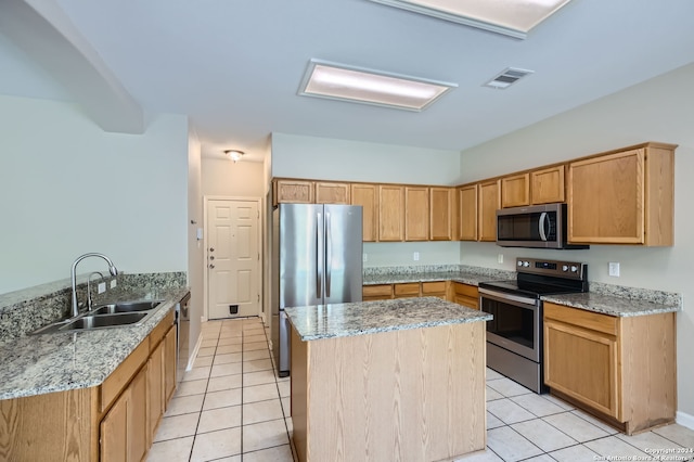 kitchen with appliances with stainless steel finishes, light stone countertops, a center island, light tile patterned floors, and sink