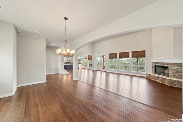 unfurnished living room with a notable chandelier, vaulted ceiling, a stone fireplace, and hardwood / wood-style flooring